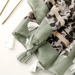 Dettaglio di sciarpa tie-dye verde salvia con trama cotone-lino e nappe bianche