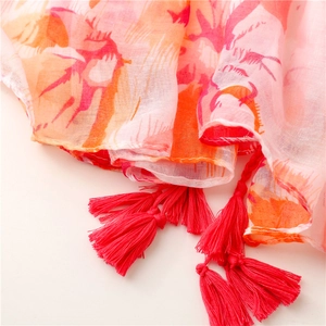Détail macro d'une écharpe rose à motifs papillons avec des pompons en soie rouge