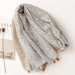 Floral cotton linen scarf with blue leaf patterns and bicolor tassels on a white surface