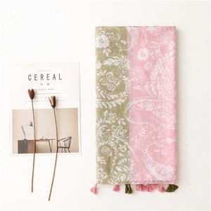 Détail d'une écharpe florale vert olive et rose avec motifs paisley et pompons décoratifs