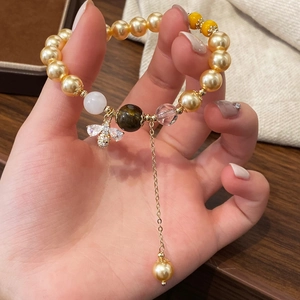 Bracelet de perles dorées avec pendentif abeille en zircon et détail de gland au poignet