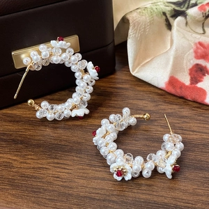 Detail of handcrafted C-shaped earrings with pearls, crystals and white flowers