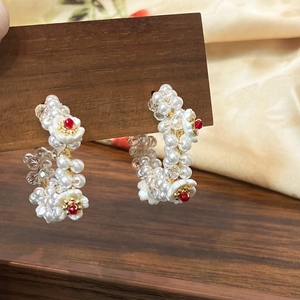 Elegant C-shaped pearl beaded hoop earrings featuring red floral accents on a wooden stand