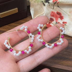 Handmade gold hoop earrings with white pearls and pink crystals shown in palm
