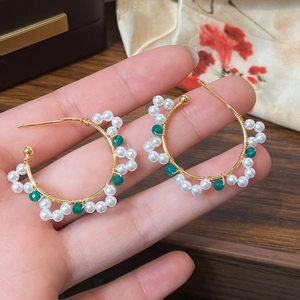 Detailed view of handmade C-shaped gold hoop earrings with white pearls and green beads