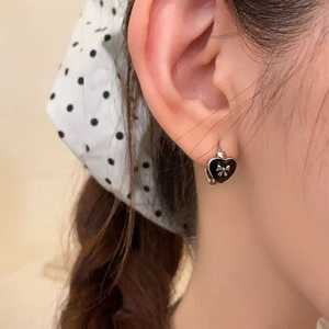 Close-up of heart-shaped black enamel earrings with silver bow worn by a model