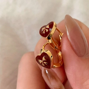 Detailed shot of red enamel heart earrings with gold bow accents and clasp design