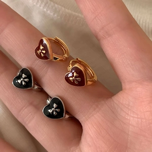 Detail of red and black enamel heart earrings with metal bow relief in hand