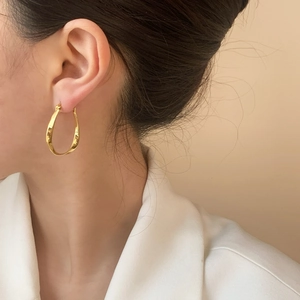 Minimalist gold spiral hoop earrings with elegant twisted oval design on a female model