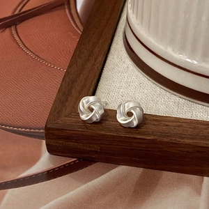 Minimalist silver twist knot earrings displayed on dark wood frame with vintage paper