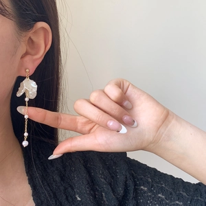 Elegant floral drop earring with white petals and pearls on a gold chain worn by a model