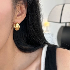 Close-up of minimalist chunky golden C-shaped hoop earrings with a matte brushed finish