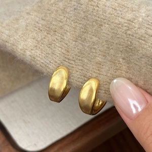 Minimalist brushed gold metal hoop earrings shown on a light brown knit sweater texture