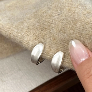 Macro view of C-shaped brushed silver earrings on soft textured beige fabric