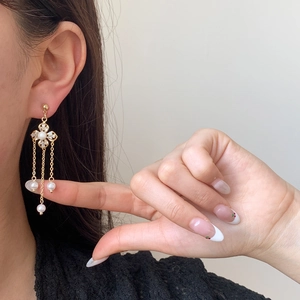 Elegant gold long tassel earrings with clover flower design and white pearls on a model