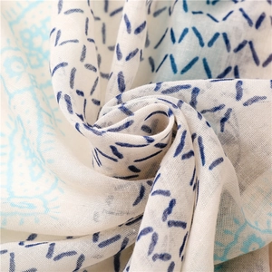 Macro detail of breathable cotton linen scarf featuring blue floral patterns and tassels