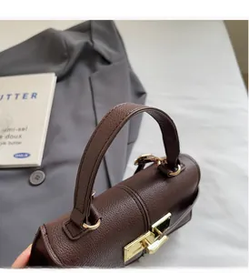 Close-up of brown litchi leather trapezoid bag featuring polished gold metal hardware buckle