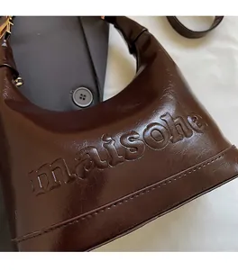Close-up of embossed MAISOHE lettering on glossy coffee brown leather pillow bag