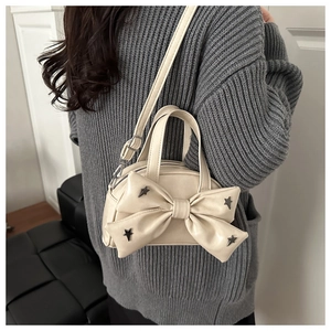 Detalle de bolso crema con lazo y remaches de estrella sobre jersey gris de punto