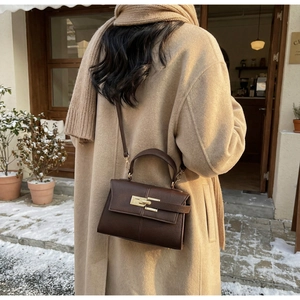 Brown litchi grain trapezoid bag with gold lock worn over a camel wool coat in winter