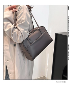 Detailed view of a dark brown minimalist tote bag on a model wearing a beige coat