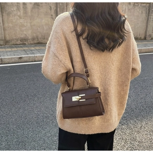 Detailed view of deep brown leather trapezoid bag with gold lock on beige sweater
