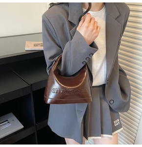 Detail of dark brown patent leather pillow bag with embossed texture and glossy finish