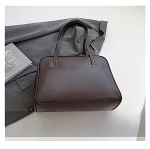 Detail of dark brown tote bag on white surface with blazer, magazine and phone accessories