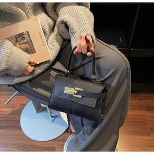 Close-up of black lychee grain leather handbag with golden metal twist-lock buckle