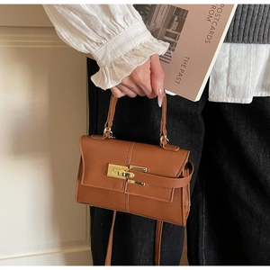 Detail of brown litchi leather handbag showing golden twist lock and textured finish