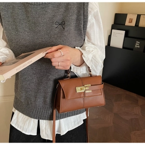 Detailed shot of brown litchi pattern leather handbag with gold buckle and top handle