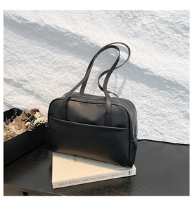 Close-up of minimalist black leather shoulder bag with silver zipper and dual long handles