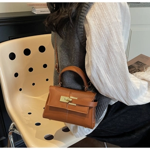Brown litchi leather trapezoid bag featuring classic metal clasp on a textured strap