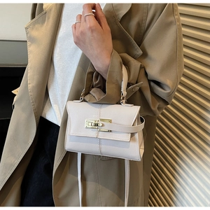 Close-up of white trapezoid handbag with gold lock on a model wearing a trench coat