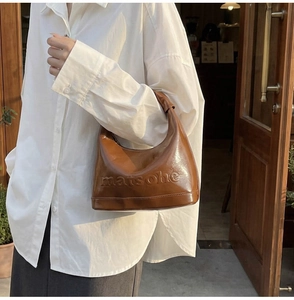Close-up of caramel leather shoulder bag with embossed matsohe lettering and smooth texture