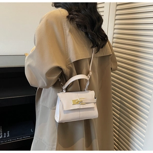 Detail shot of the elegant white leather trapezoid handbag with a gold lock on a model