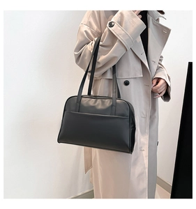 Minimalist black matte leather tote bag styled with a beige coat in a clean setting