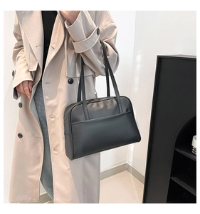 Detail of minimalist black matte leather tote bag worn with a beige trench coat