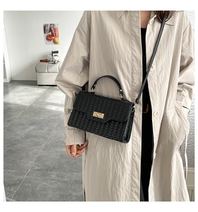 Detailed view of black woven texture handbag with gold swivel lock on a beige coat