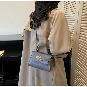 Detail of grey lychee leather trapezoid handbag with gold clasp worn with a beige coat