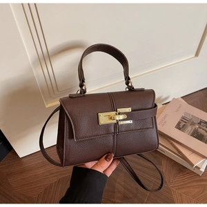 Detail of brown lychee grain leather texture and golden metal clasp on trapezoid bag