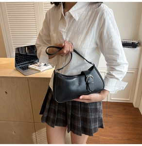Detail of black leather underarm bag with silver buckle worn with a white casual shirt