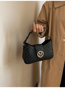 Close-up of black baguette bag featuring M-pattern print and a large golden circular buckle