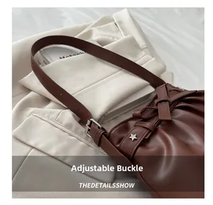 Detail of brown pleated shoulder bag showing adjustable strap buckle and star rivet