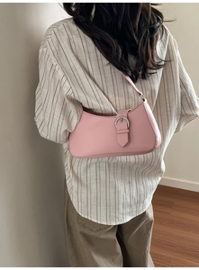 Close-up of a light pink crescent hobo bag featuring a metallic buckle on a shoulder model