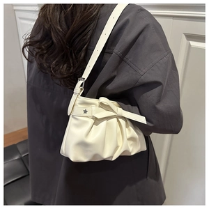 Detail of cream pleated tote bag featuring a decorative bow and star charm on shoulder strap