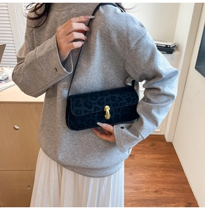 Détail du sac baguette léopard en velours avec boucle dorée porté à l'épaule de femme