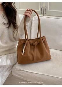 Dettaglio di una borsa tote in pelle marrone con fibbia decorativa e ciondolo in legno