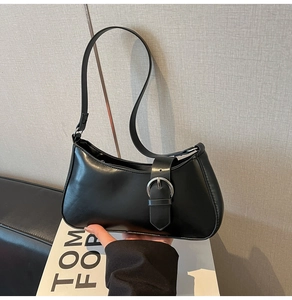 Detail of minimalist black leather shoulder bag with a large silver metal buckle strap