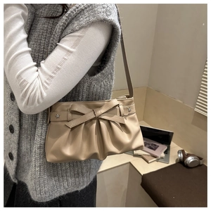 Close-up of beige pleated tote bag with bow detail and star studs on a laptop background
